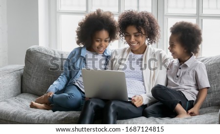Young African mother with little daughter and son sitting on couch with laptop using on-line websites, buying choosing goods, mommy teach children online, education or having fun in internet concept
