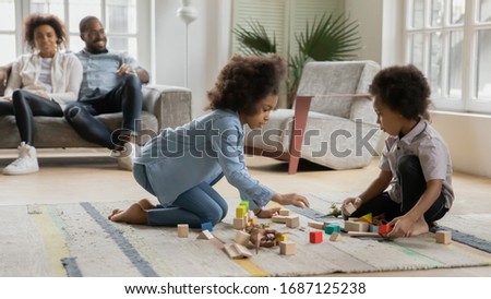 Children play on floor with wooden blocks dino set parents sit on sofa resting at new home first dwelling, cozy rented house. Investment in future, flat remodeling, weekend activity with kids concept Royalty-Free Stock Photo #1687125238