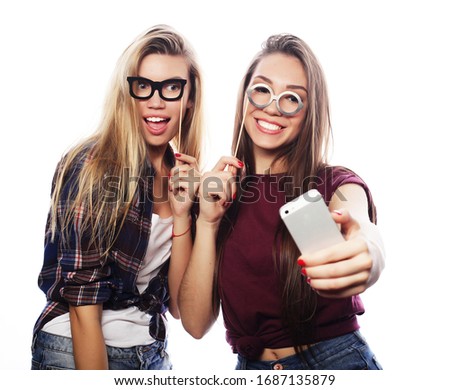 two young happy women with party glasses taking selfie with mobile over white background