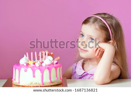 A little blonde girl with a pink cake with candles. Birthday. Isolated pink background. The girl looks away. Party 6 years.