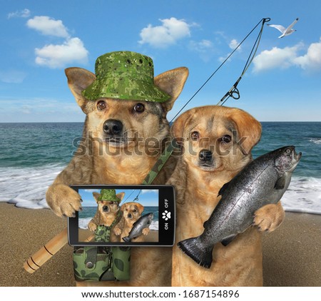 Two dogs fishers are on a beach of the sea. One of them holds a caught fish, the other with a fishing bag and a fishing rod holds a smartphone. They made selfie. 