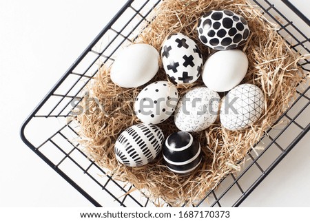 Top view of an iron mesh basket with a nest of hay with black and white minimalistic painted eggs. Easter in modern style concept. Advertising space