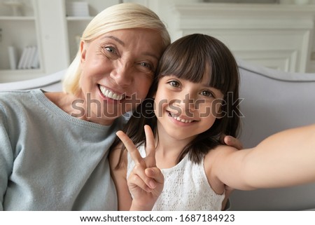 Close up portrait of happy little preschooler girl and senior grandmother take selfie on smartphone together, overjoyed mature grandparent have fun make self-portrait picture with small granddaughter