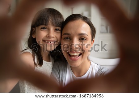 Close up portrait of little girl and young mom or nanny have fun make selfie with heart hand gesture, smiling mother play with small preschooler daughter take self-portrait picture at home together Royalty-Free Stock Photo #1687184956