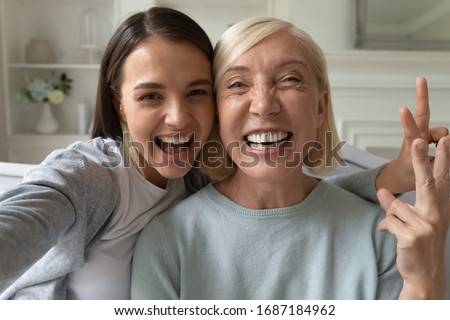 Smiling millennial girl child take selfie with overjoyed funny elderly mother at home, happy grown-up adult daughter have fun make self-portrait picture with mature mom, relax together on weekend