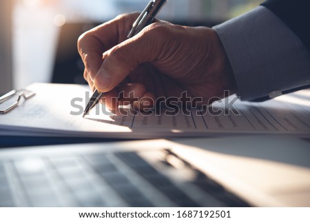 Businessman, executive manager hand filling paper business document, signing contract, partnership agreement and working on laptop computer on desk in modern office, close up Royalty-Free Stock Photo #1687192501