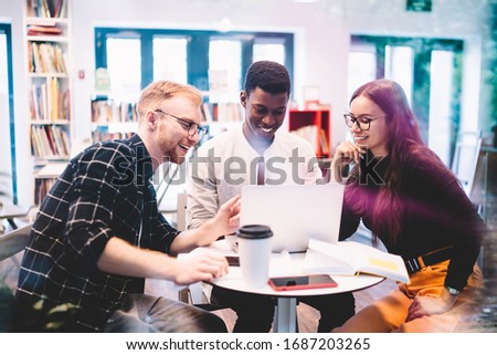 Happy multicultural hipster guys browsing dunny web articles during laptop networking in university campus, cheerful male and female millennials searching positive medial files on computer