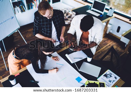 African American male coworker taking pictures of blueprint sketch during cooperation time with smart casual colleagues, young millennial creating design project in modern workspace of university