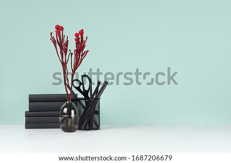 Minimalistic style home workplace with black stationery, books, red branch on green mint menthe wall and white wood table.