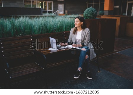 Cheerful caucasian female watching video on laptop computer sitting on college campus, smiling hipster girl earning online enjoying remote job and share publications in social networks and web site 