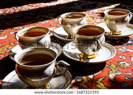 vintage soviet porcelain cups of tea with saucers on turkish carpet, traditional tea ceremony, sunlight with deep shadows
