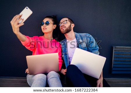 Male and female friends shooting influence video vlog for create media content and share to social web blog, millennial freelancers working remotely with laptop clicking selfie pictures on cellphone