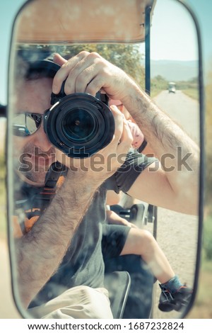 Israeli man reflected on the side mirror of an electric golf cart while taking a self portrait picture. He traveling in the countryside of Israeli Hula Valley in summer day. Close up & selective focus