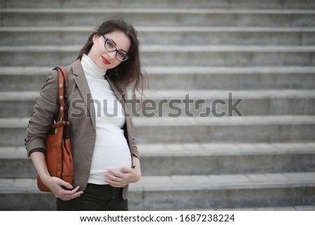 Pregnant woman talking on the phone in the street near the building
