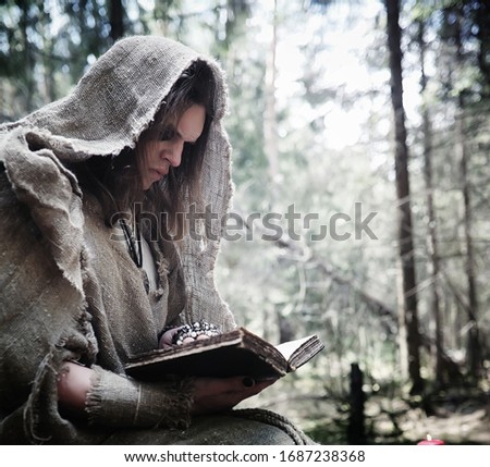 Fairy magician. A sorcerer with a glass sphere, a magical spell and a ritual. Elder with a staff and a cross in the forest. Black and white magic. A spell in old book.
