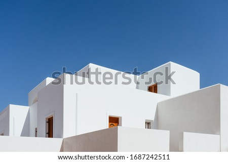 Minimal buildings background with traditional Greek style architecture. Low angle view of white houses against a blue clear summer sky. Outdoor estate construction of modern residential building.  Royalty-Free Stock Photo #1687242511