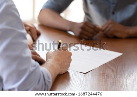 European couple during meeting with african ethnicity realtor signing rental agreement close up image, client buying first property hold pen put signature on legal paper document, make deal concept Royalty-Free Stock Photo #1687244476
