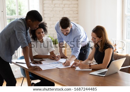Caucasian team leader share project idea to multi-ethnic workmates, workgroup brainstorming discussing planning corporate strategy, doing paperwork, reviewing financial data at office meeting concept Royalty-Free Stock Photo #1687244485