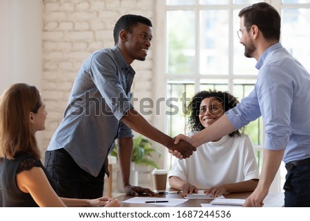Before start negotiations African and Caucasian businessmen partners greets each other shake hands express respect friendly attitude. Closing deal, reach agreement, congratulate to promoted employee Royalty-Free Stock Photo #1687244536