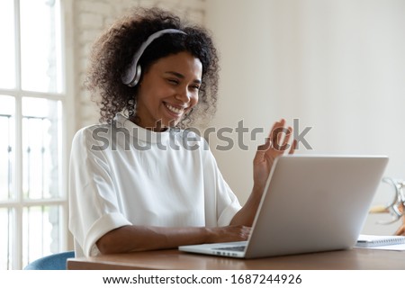 African tutor of language start on-line lesson with trainee wave hand smiling looks at pc screen. Mixed-race woman in headphones communicating distantly, e-learning process, application usage concept Royalty-Free Stock Photo #1687244926