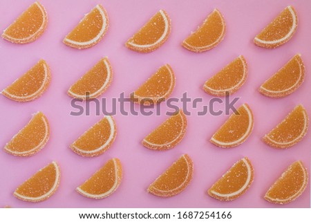 Marmalade slices of orange laid in oblique rows on a pink background
