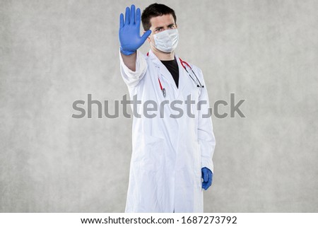  a doctor in protective clothing shows a stop sign with his hand