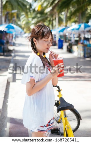 Young asian cute on white shirt girl drinking red sweet soda from plastic cup with straw at the beach.