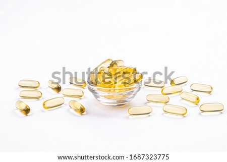 Bunch of omega 3 fish liver oil capsules in small glass bowl. Close up of golden translucent pills in pile. Healthy every day fatty acids nutritional supplement dosage. Top view, flat lay, copy space.