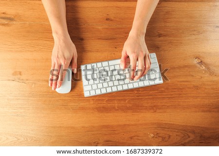 Female hands working with modern white keyboard and mouse on wooden background, top view 