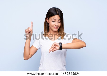 Young woman over isolated blue background looking at the hand watch Royalty-Free Stock Photo #1687345624