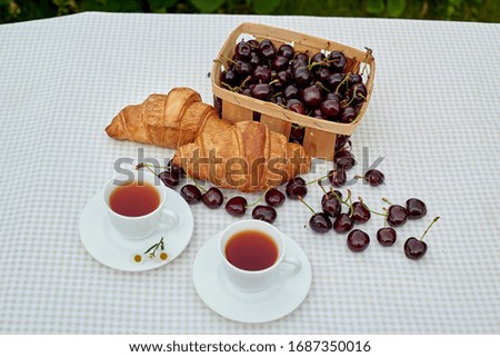 
Black tea with fresh croissants and cherries on the table against white background. Flat lay, spring breakfast conceptual composition