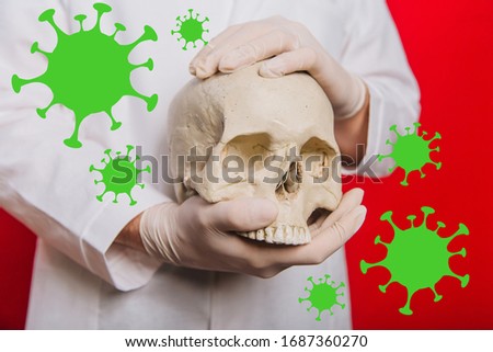 Doctor's hands in gloves hold a human skull on a red background. Coronaviruses fly in the air. Photo Illustration of the epidemic COVID-19. Pandemic death