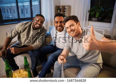 friendship, leisure and people concept - male friends taking picture with selfie stick and drinking beer at home