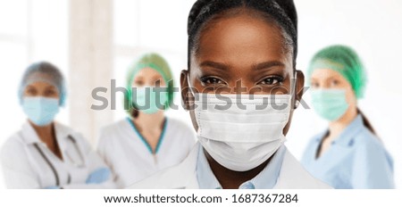 health, medicine and pandemic concept - close up of african american female doctor or scientist in protective mask over medical workers at hospital on background Royalty-Free Stock Photo #1687367284