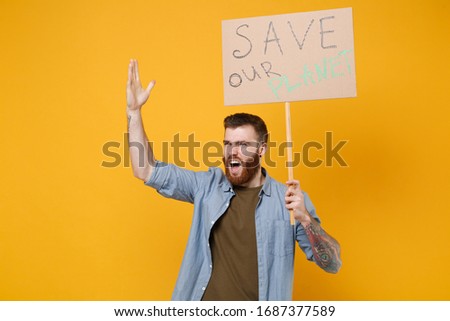 Irritated young protesting man hold protest sign broadsheet placard on stick rising hand scream isolated on yellow background. Stop nature garbage ecology environment protection concept. Save planet
