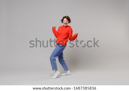 Side view of joyful young woman girl in casual red hoodie blue jeans posing isolated on grey background. People lifestyle concept. Mock up copy space. Clenching fists like winner keeping eyes closed Royalty-Free Stock Photo #1687385836