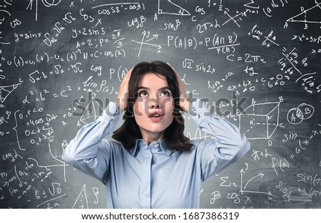 Portrait of shocked young woman college student standing near blackboard with formula written on it concept of education, maths and science