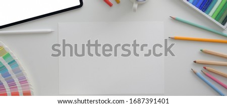 Overhead shot of designer workplace with mock-up tablet, sketch paper and designer supplies on white desk  