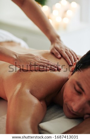 Practitioner using both hands to deliver a long gliding stroke from the base of the lumbar region towards the shoulders and neck Royalty-Free Stock Photo #1687413031
