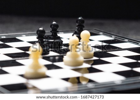 a chessboard on it stands three black and white pawns on black concrete a dark background. copy space