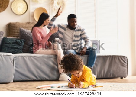 Focus on girl draws on the floor. Parents arguing in background