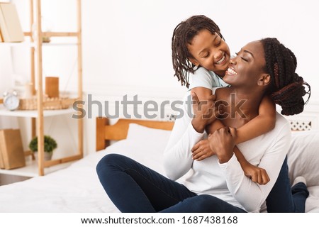 Togetherness Concept. African daughter hugging her mum from the back, sitting on bed, showing her love, empty space Royalty-Free Stock Photo #1687438168
