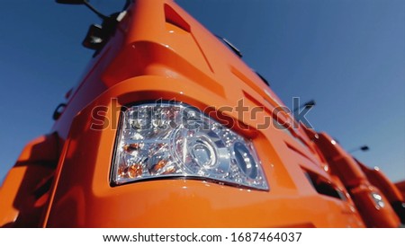Close up of the side part of the truck body of red color and front headlight on blue clear sky background. Stock footage. New truck details, construction concept.