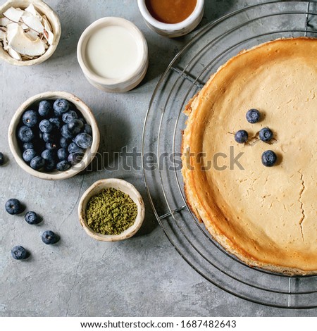 Homemade cane sugar baked cheesecake on cooling rack with variety of toppings in ceramic bowls over grey texture background. Flat lay, space