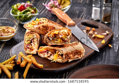 Shawarma chicken roll in a pita with fresh vegetables, cream sauce and french fries on wooden background. Selective focus Royalty-Free Stock Photo #1687518595