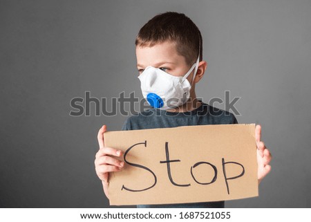 boy, a child in a protective mask on his face, looking at the camera, holding a stop sign. Air pollution, virus, Chinese pandemic coronavirus concept.