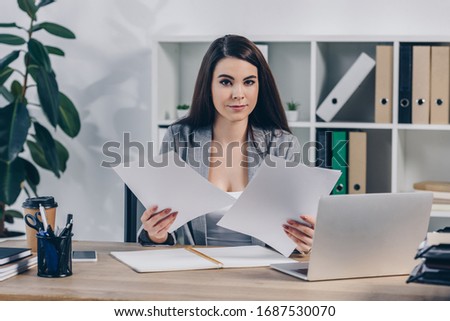 Recruiter with papers and laptop looking at camera at table in office