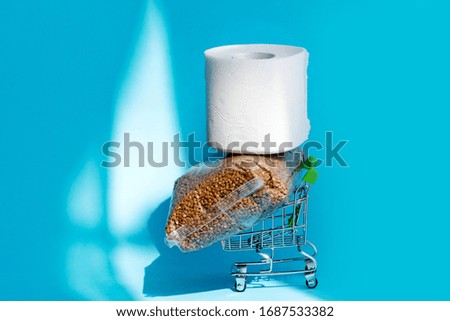 Buckwheat and toilet paper on a shopping cart  on blue background. Consumer buying panic about coronavirus covid-19 concept. Stocking up essentials for home quarantine
