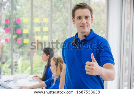 Customer support operator at work. Team Business and Delivery call center in office. Working with a headset in blue uniform while showing thumbs up.