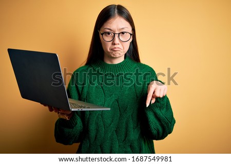 Young asian business woman wearing glasses and working using computer laptop Pointing down looking sad and upset, indicating direction with fingers, unhappy and depressed.